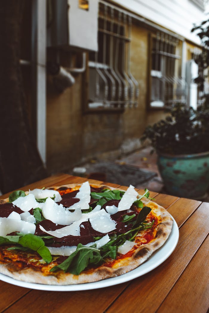 Close-up of a rustic artisan pizza topped with fresh spinach and cheese, set on a wooden table outdoors.