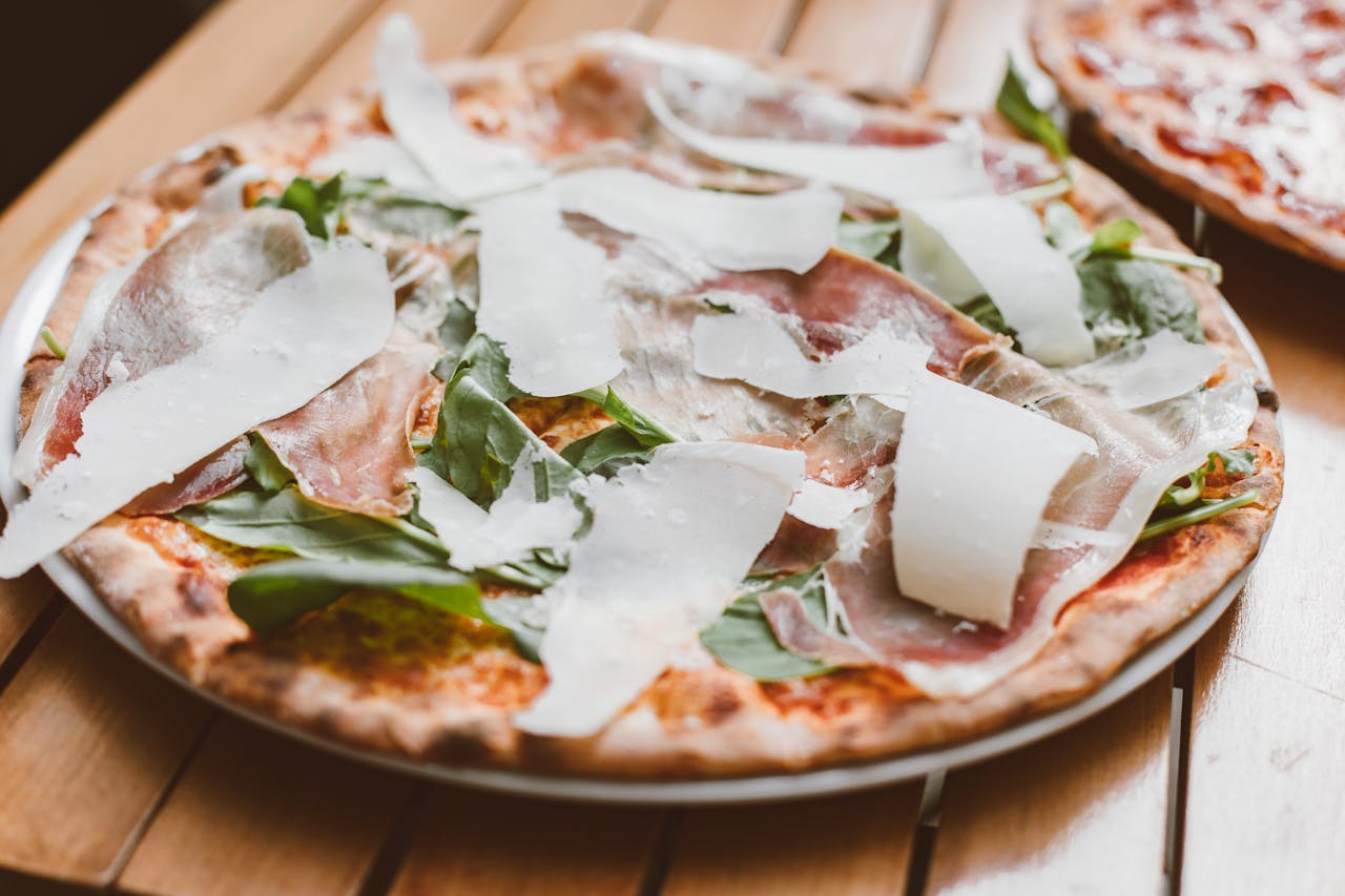 Close-up of a freshly baked Italian pizza topped with prosciutto, arugula, and Parmesan cheese.